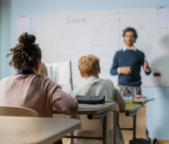 Alunos atentos em sala de aula enquanto professor explica conteúdo no quadro, representando aprendizado e educação