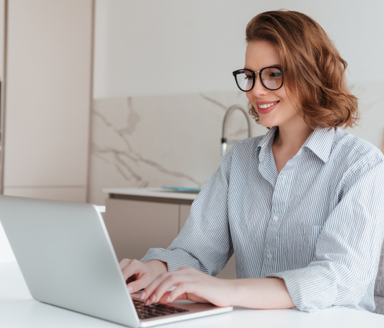 Mulher sorridente usando óculos trabalhando em um laptop em casa, representando home office e produtividade