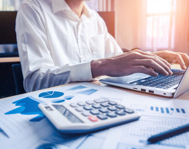 Profissional analisando relatórios financeiros e gráficos em um laptop, com calculadora sobre a mesa, representando contabilidade e gestão financeira